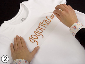 Das Strassmotiv liegt mit seiner Trägerfolie ausgerichtet auf dem Shirt.