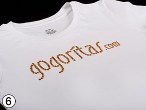 Fertiger orangefarbener Gogoritas-Schriftzug aus Strass auf einem weißen Shirt.