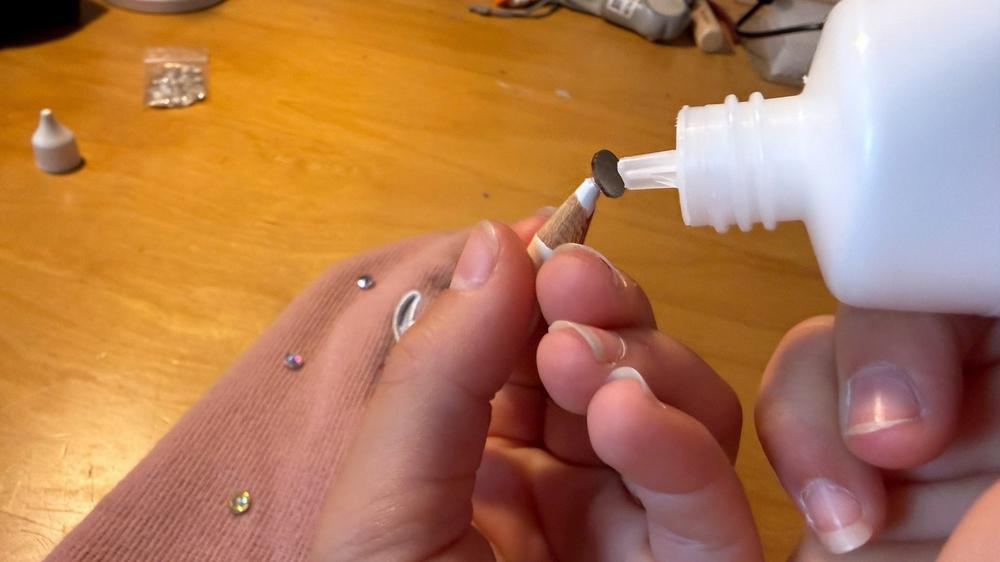 Ein kleiner Kleberpunkt wird auf die flache Rückseite eines Strasssteins aufgetragen.